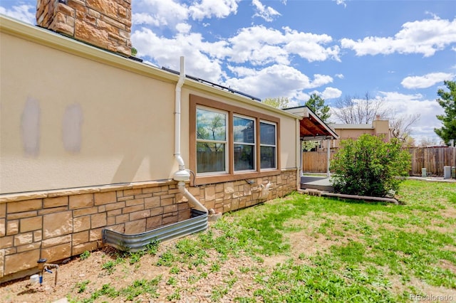 view of home's exterior featuring stucco siding, stone siding, and fence