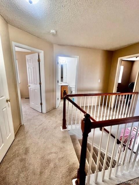 corridor with a textured ceiling and light colored carpet