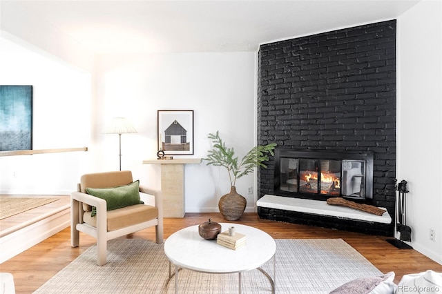 living area with a brick fireplace, wood finished floors, and baseboards