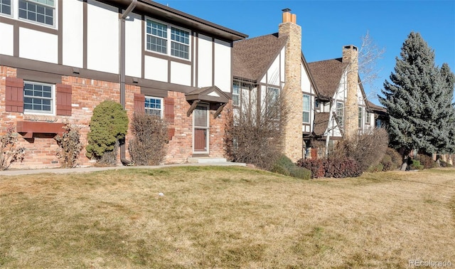 english style home with stucco siding, a front yard, and brick siding