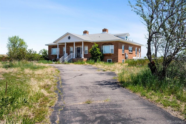 greek revival house featuring brick siding, a chimney, driveway, and covered porch
