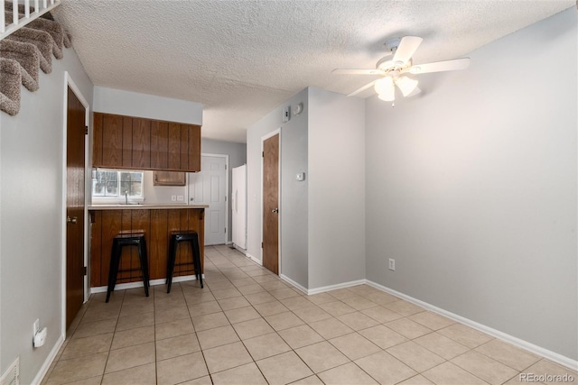 kitchen featuring a kitchen bar, sink, a textured ceiling, kitchen peninsula, and ceiling fan