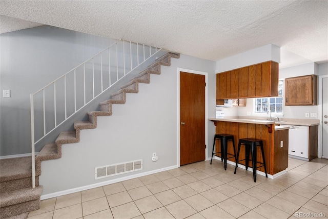 kitchen with light tile patterned flooring, a breakfast bar area, white dishwasher, and kitchen peninsula