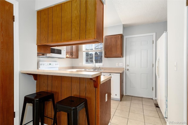 kitchen with light tile patterned floors, white appliances, a breakfast bar area, and kitchen peninsula