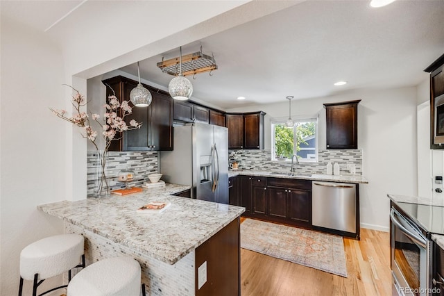 1765 Xenia St, Denver, CO 80220 - kitchen with appliances with stainless steel finishes, a sink, dark brown cabinetry, a peninsula, and light wood-style floors