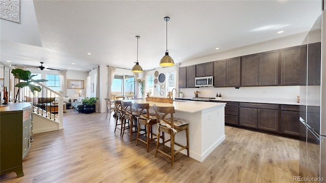 689 Olive St, Broomfield, CO 80023 - kitchen featuring appliances with stainless steel finishes, a kitchen island with sink, dark brown cabinetry, and light wood finished floors