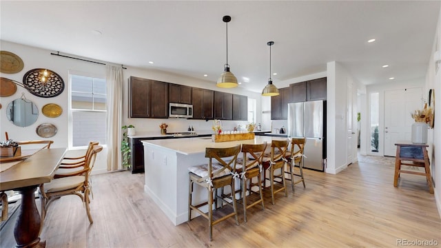 689 Olive St, Broomfield, CO 80023 - kitchen featuring dark brown cabinetry, a kitchen island, appliances with stainless steel finishes, light wood finished floors, and a breakfast bar area