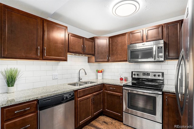 kitchen with sink, dark hardwood / wood-style floors, light stone countertops, appliances with stainless steel finishes, and tasteful backsplash