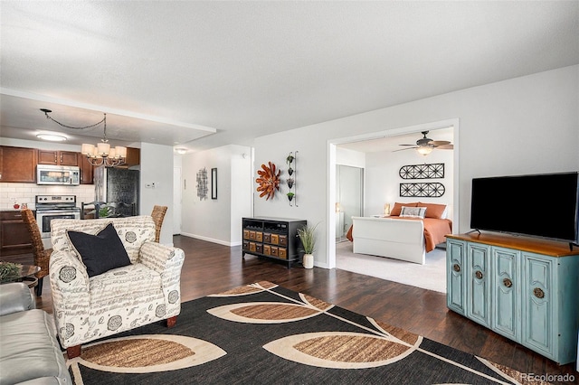 living room with ceiling fan with notable chandelier, dark wood-type flooring, and baseboards