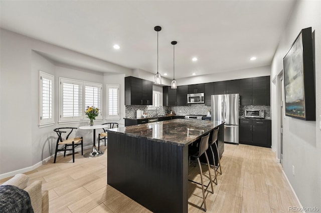 10793 Alcott Way, Denver, CO 80234 - kitchen featuring dark cabinets, stainless steel appliances, tasteful backsplash, a kitchen breakfast bar, and a center island