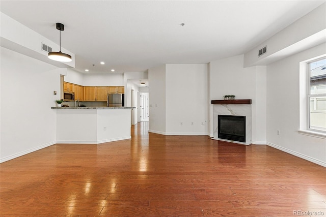 unfurnished living room with visible vents, baseboards, hardwood / wood-style floors, and a high end fireplace