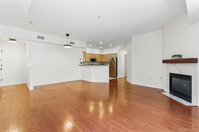 unfurnished living room with a fireplace, visible vents, light wood finished floors, and baseboards