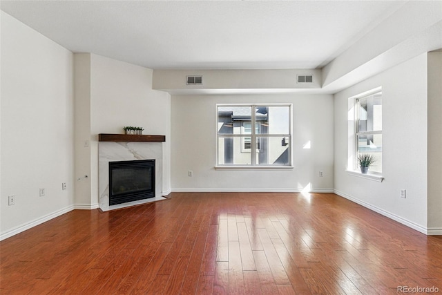 unfurnished living room featuring visible vents, a premium fireplace, and hardwood / wood-style flooring