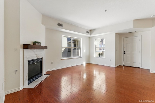 unfurnished living room featuring a tiled fireplace, visible vents, baseboards, and wood-type flooring