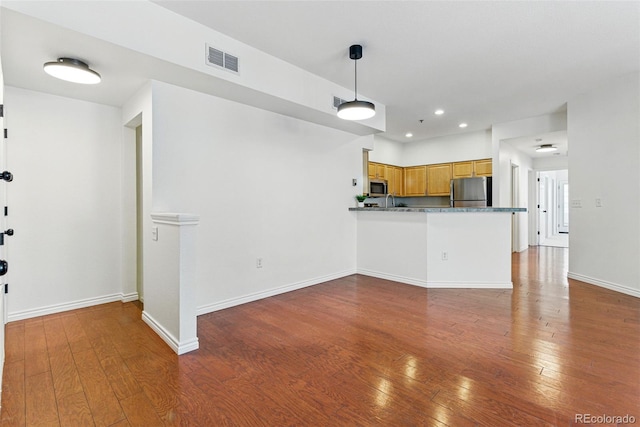 kitchen featuring visible vents, baseboards, hardwood / wood-style floors, brown cabinets, and stainless steel appliances