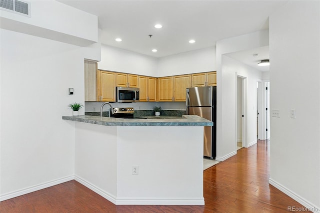 kitchen featuring visible vents, wood finished floors, stainless steel appliances, a peninsula, and baseboards