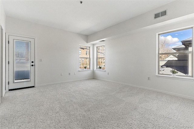 carpeted spare room with a wealth of natural light, visible vents, and baseboards