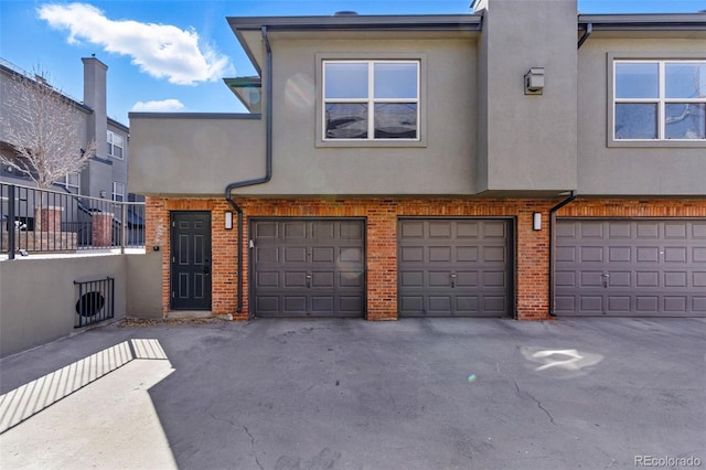 exterior space with stucco siding, brick siding, and an attached garage