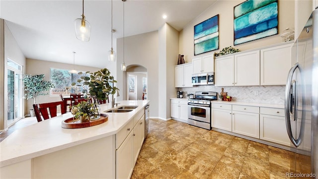 kitchen with backsplash, an island with sink, appliances with stainless steel finishes, arched walkways, and a sink