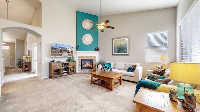 carpeted living area featuring arched walkways, ceiling fan, a tile fireplace, and a towering ceiling