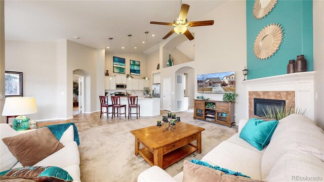 living room with a ceiling fan, a fireplace, arched walkways, and high vaulted ceiling