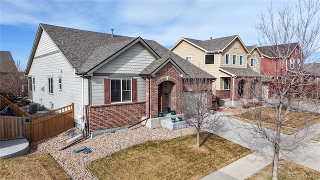 view of front of home with brick siding, a shingled roof, a front lawn, fence, and central air condition unit