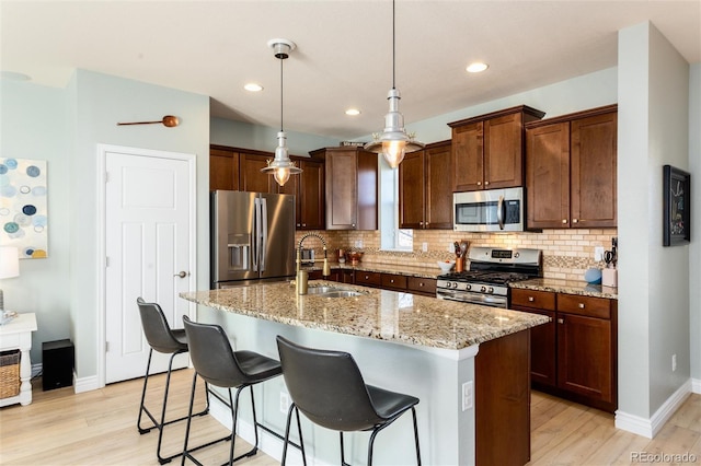 kitchen with light wood finished floors, tasteful backsplash, appliances with stainless steel finishes, a sink, and light stone countertops