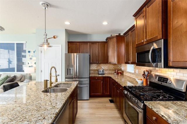 kitchen featuring stainless steel appliances, backsplash, light wood-style flooring, a sink, and light stone countertops