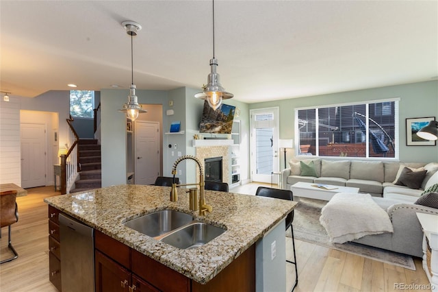 kitchen with a fireplace, a sink, open floor plan, light wood-type flooring, and dishwasher