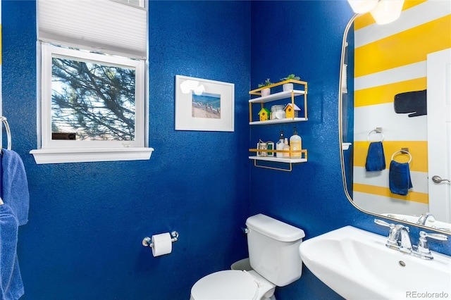 half bathroom with a textured wall, a sink, and toilet