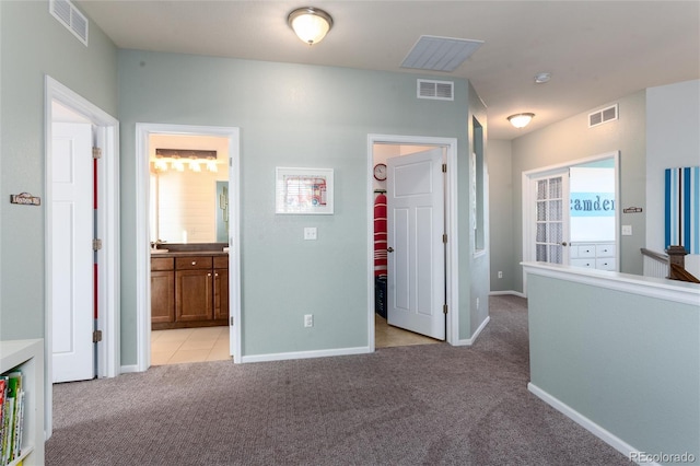 hall featuring baseboards, visible vents, and light colored carpet