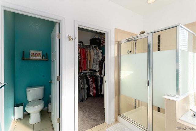 bathroom with a stall shower, a walk in closet, tile patterned flooring, and toilet