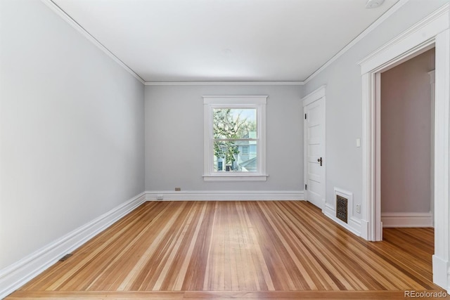 empty room with crown molding, light wood finished floors, baseboards, and visible vents