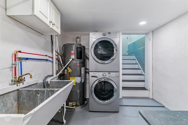 washroom featuring stacked washer and dryer, cabinet space, a sink, hybrid water heater, and a textured wall