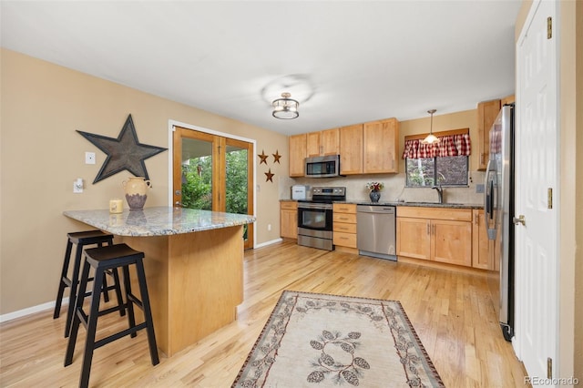 2871 Humboldt Cir, Longmont, CO 80503 - kitchen with stainless steel appliances, a peninsula, a kitchen bar, light wood-style flooring, and light stone counters