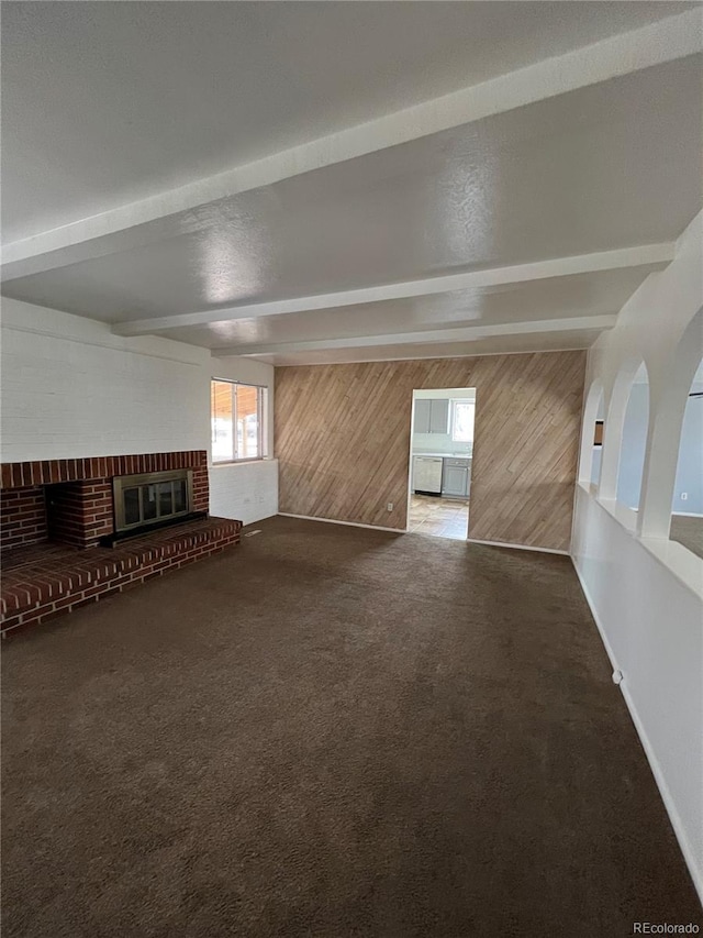 interior space featuring a fireplace, dark carpet, beam ceiling, and wooden walls