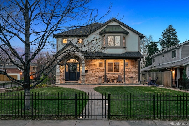 view of front facade with a front lawn, a fenced front yard, covered porch, and stone siding