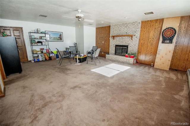 unfurnished living room with a textured ceiling, wooden walls, ceiling fan, carpet flooring, and a brick fireplace