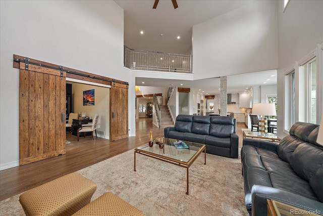 living room with a ceiling fan, wood finished floors, a barn door, stairway, and a high ceiling