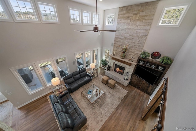 living room featuring a stone fireplace, a high ceiling, ceiling fan, and wood finished floors