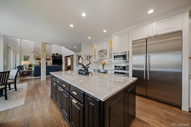 kitchen featuring wood finished floors, built in appliances, white cabinets, and light stone countertops