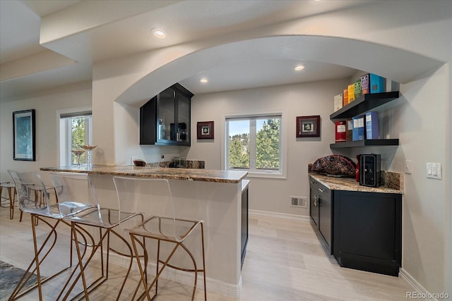 kitchen with light stone counters, open shelves, a kitchen breakfast bar, and dark cabinets