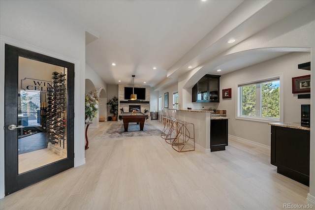 kitchen with light wood finished floors, a kitchen breakfast bar, a large fireplace, and light stone counters