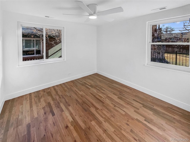 empty room with ceiling fan, wood finished floors, visible vents, and baseboards