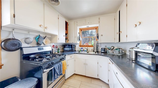 kitchen featuring black microwave, stainless steel gas range oven, tasteful backsplash, a sink, and white cabinetry