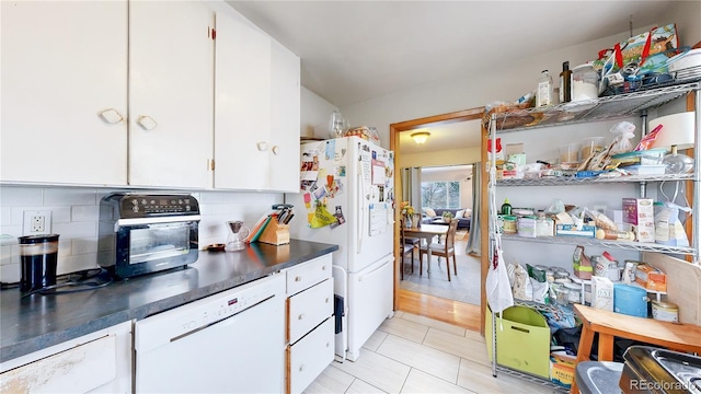 kitchen with dark countertops, white appliances, white cabinetry, light tile patterned floors, and backsplash