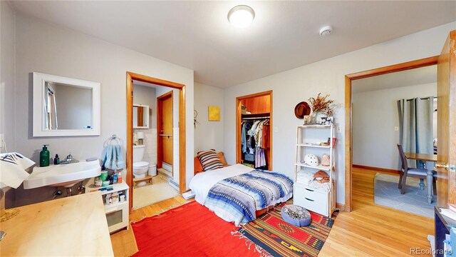 bedroom with wood finished floors, a sink, a closet, connected bathroom, and a spacious closet