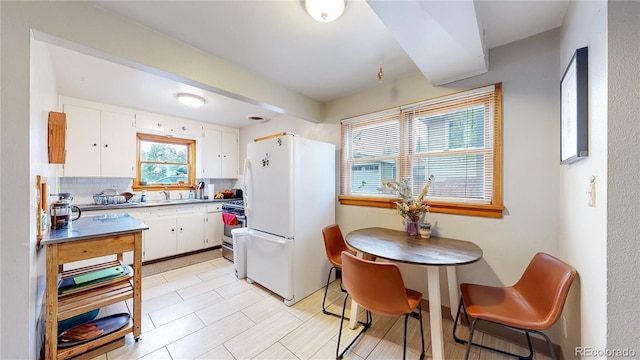 kitchen with gas stove, white cabinets, freestanding refrigerator, and a sink