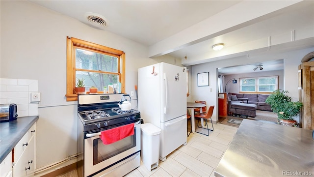 kitchen featuring visible vents, freestanding refrigerator, stainless steel range with gas cooktop, white cabinets, and stainless steel countertops