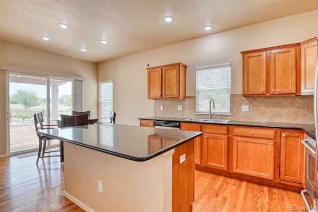 kitchen with a kitchen island, tasteful backsplash, sink, dark stone counters, and light hardwood / wood-style floors